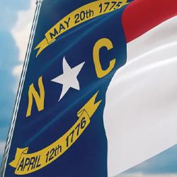 A North Carolina state flag blows in the wind in front of a blue sky